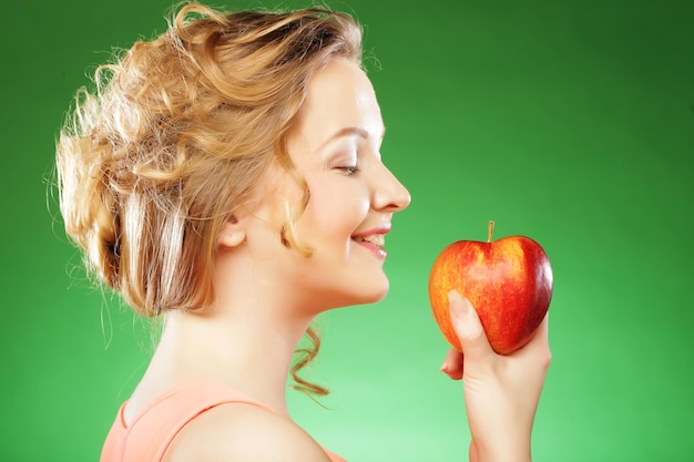 Belle femme tenant une pomme à côté de sa bouche sur fond vert