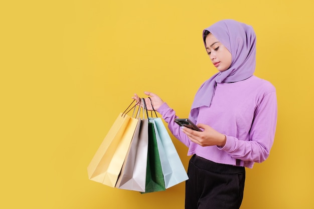 Belle femme tenant des sacs à provisions, bien et de bonne humeur, à l'aide de téléphone mobile