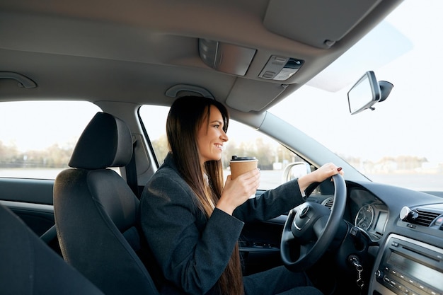 Belle femme tenant le volant et la tasse de café tout en conduisant une voiture vue rapprochée