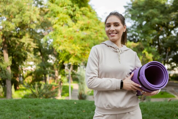 Belle femme tenir le tapis pour les exercices de sport dans les mains avant l'entraînement en plein air