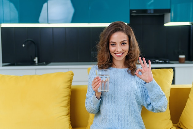 Belle femme tient un verre d'eau pure et montre un signe ok à la main à la maison. Concept de mode de vie et concept sain.