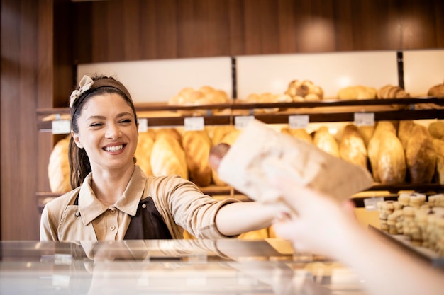 Belle femme travaillant dans une boulangerie et vendant des pâtisseries savoureuses fraîches au client