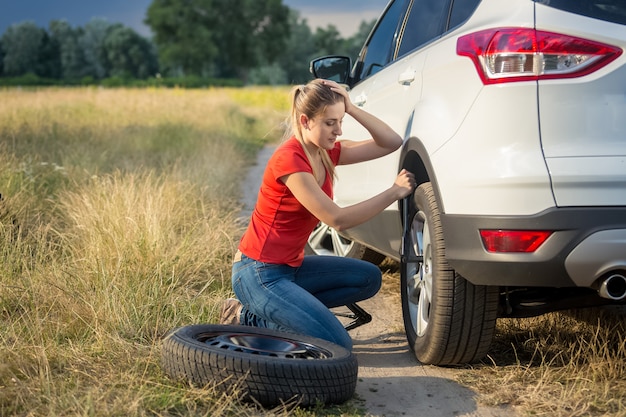 Une belle femme triste s'est trompée sur le changement de pneu crevé sur le terrain