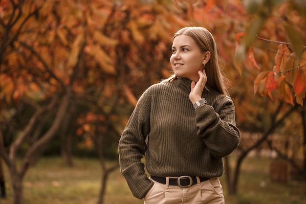 Belle femme ukrainienne blonde dans un chandail tricoté vert et un jean clair dans un parc d'automne avec des orangers Automne doré