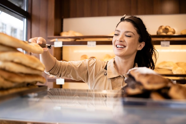 Belle femme en uniforme travaillant dans une boulangerie et vendant des pâtisseries au client