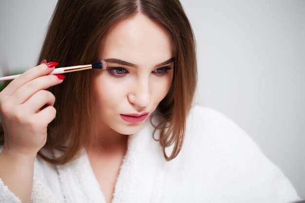 Belle femme utilisant une brosse pour le maquillage quotidien dans la salle de bain