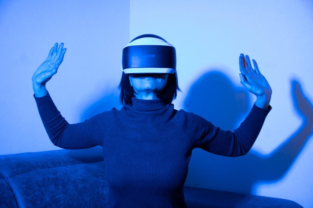 Belle femme utilisant un casque vr dans un espace virtuel à la maison à la lumière bleue. Le concept de l'univers virtuel. Style de vie dans l'espace virtuel