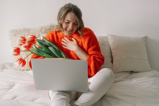 Belle femme utilisant un ordinateur portable au lit à la maison. Femme se réjouir des tulipes