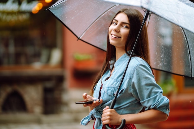 Belle femme utilisant un smartphone dans la rue par temps de pluie souriant tenant un parapluie pluie d'été