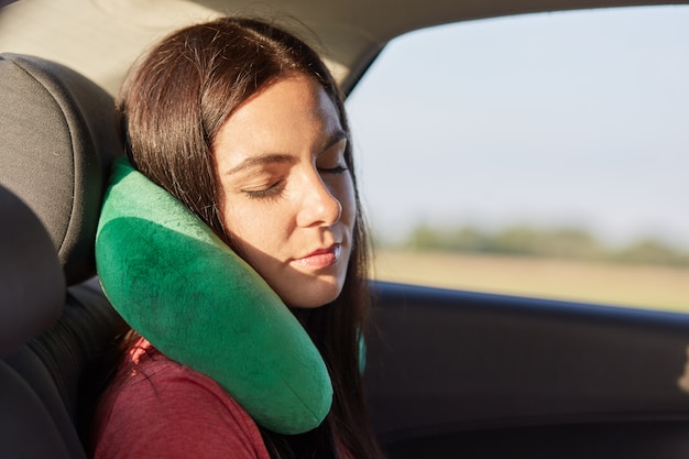 Une belle femme utilise un oreiller cervical pour dormir dans la voiture, voyage sur de longues distances, essaie de se détendre, ressent une douleur dans le cou pour être dans une position pendant longtemps. Gens, voyages, confort, concept de voyage