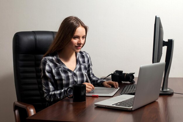 Belle femme va faire son travail de retouche assis sur la chaise à l'aide d'un ordinateur portable au bureau