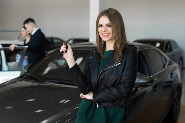 Belle femme ou vendeur de voiture stand tenant une nouvelle clé à distance de voiture dans une salle d'exposition de voiture