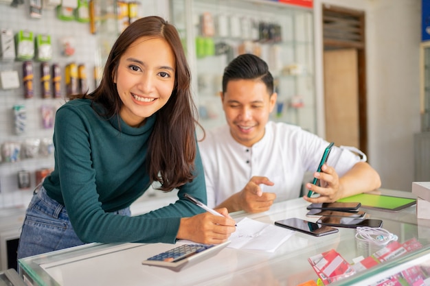 Belle femme vendeuse souriante tout en travaillant avec un homme vérifiant le papier à lettres avec des notes...