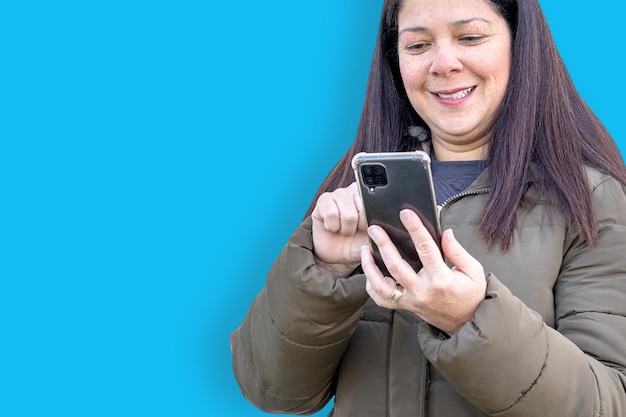 Belle femme vérifiant son téléphone portable souriant à la bonne nouvelle reçue sur fond bleu clair