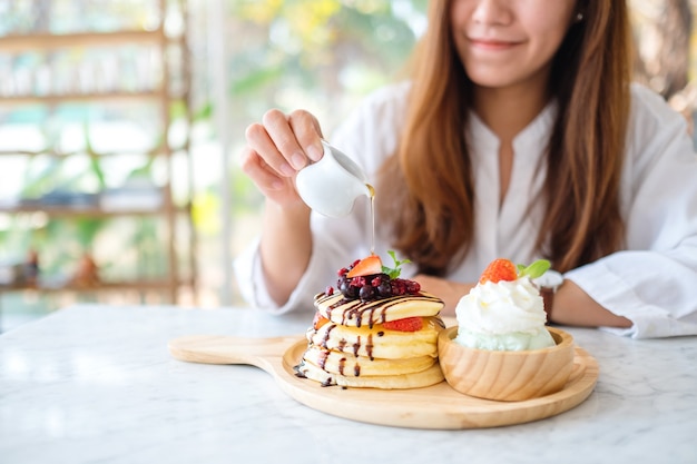 Une belle femme versant du miel dans un morceau de crêpes aux baies mélangées avec de la crème glacée et de la crème fouettée