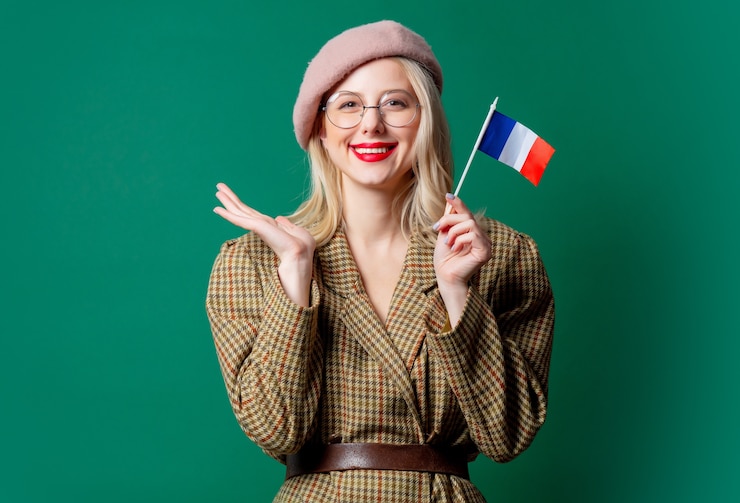 Photo belle femme en veste de style et chapeau avec drapeau français sur mur vert