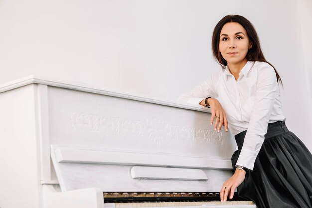 Belle femme vêtue d'une chemise blanche jouant au piano blanc. Place pour le texte ou la publicité