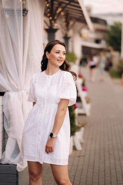 Une belle femme vêtue d'une robe blanche au coucher du soleil dans la ville Photographie de rue en soirée