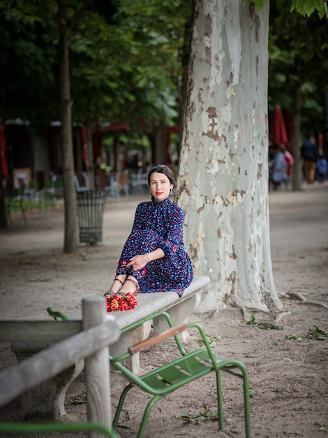 Belle femme vêtue d'une robe bleu foncé assise sur une chaise dans le parc