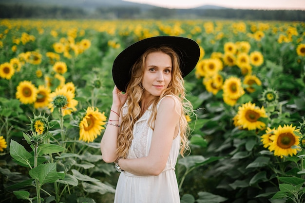 Belle femme vêtue d'une robe légère se promène parmi les tournesols dans le champ