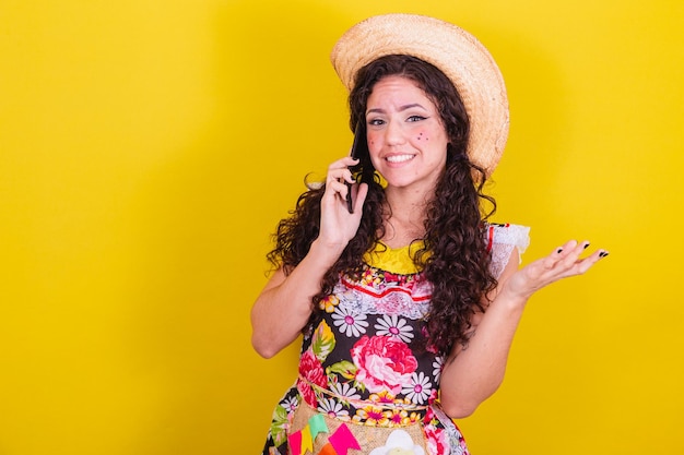 Belle femme vêtue de vêtements typiques pour une Festa Junina parlant par appel audio sur téléphone portable