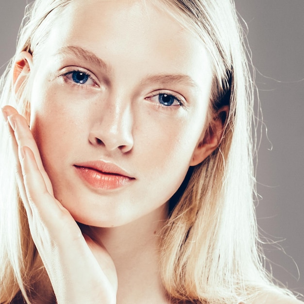 Belle femme visage Portrait Beauté Soins de la peau Concept.avec les mains Mannequin de beauté avec de beaux cheveux sur fond gris. Prise de vue en studio.