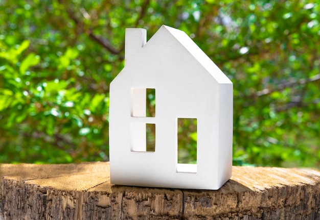 Belle figurine d'une maison blanche sur un fond en bois avec des feuilles vertes derrière