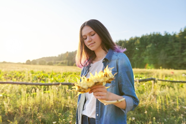 Belle fille adolescente souriante avec tournesol plante avec graines mûres. Paysage de campagne pittoresque, heure d'or, espace de copie