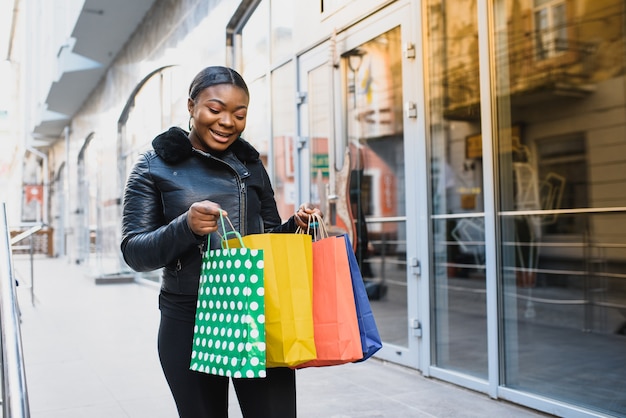 Belle fille afro-américaine aux cheveux bouclés foncés debout avec des sacs à provisions dans ses mains.