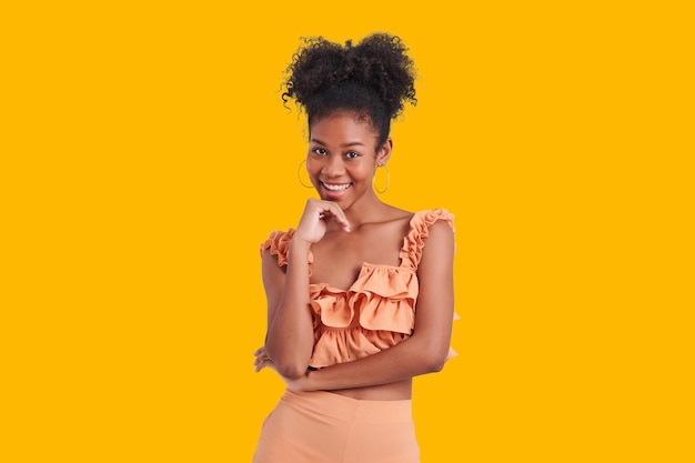 Belle fille afro-américaine avec une chemise orange porter une coiffure afro souriante charmant fond de couleur jaune isolé