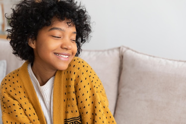 Belle fille afro-américaine avec une coiffure afro souriante assise sur un canapé à la maison intérieure jeune afr