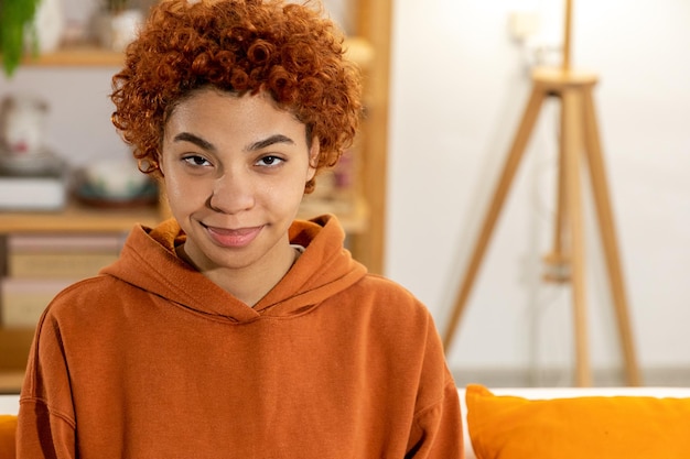 Belle fille afro-américaine avec une coiffure afro souriante assise sur un canapé à la maison intérieure jeune afr