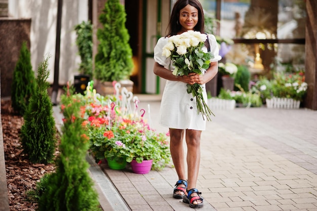 Belle fille afro-américaine tenant un bouquet de fleurs de roses blanches sur la datation dans la ville Femme d'affaires noire avec bouquet de fleurs