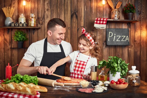 Belle fille aidant papa à répandre la sauce pendant la cuisson de la pizza