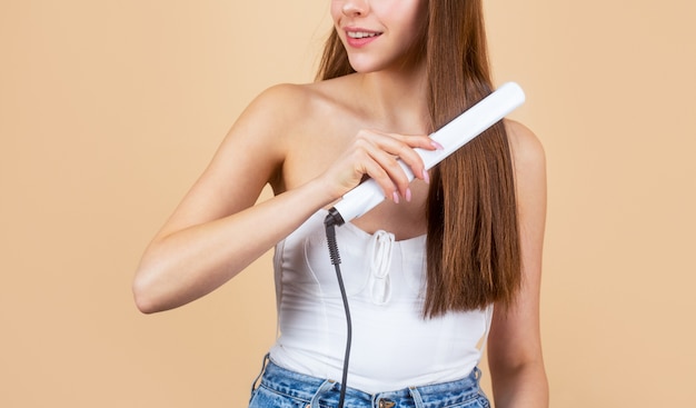 Belle fille à l'aide de styler sur ses cheveux brillants.