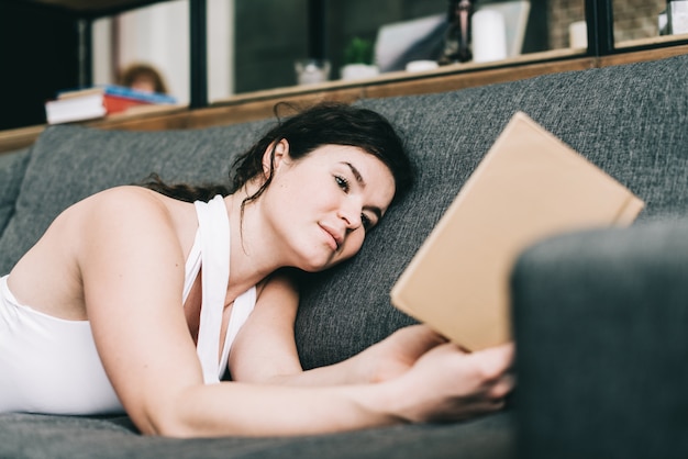 Belle fille allongée sur le canapé et en lisant un livre