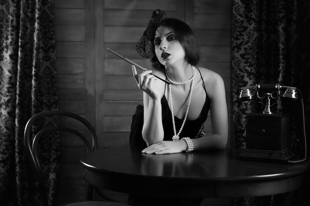 Belle fille des années 1930 fume une cigarette à la table