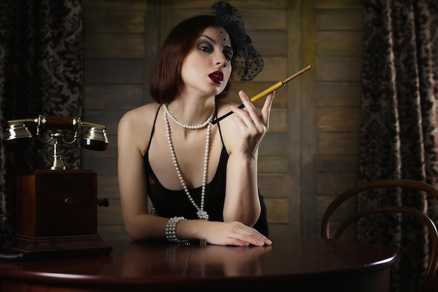 Belle fille des années 30 fume une cigarette à la table