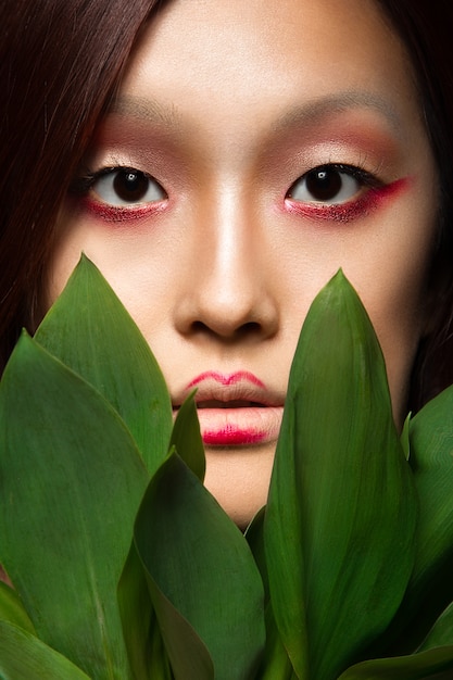 Belle fille asiatique avec un art de maquillage lumineux dans des feuilles vertes.