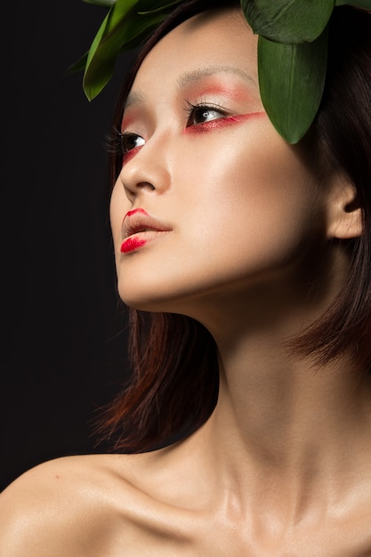 Belle fille asiatique avec un art de maquillage lumineux dans des feuilles vertes.