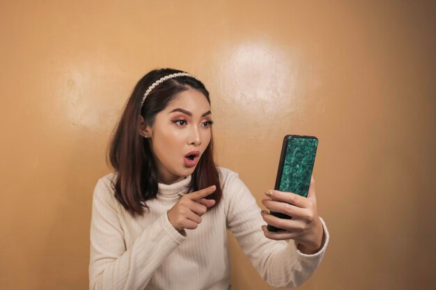 La belle fille asiatique est choquée dans le smartphone avec la chemise blanche