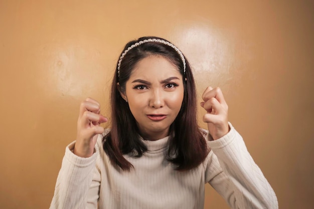 Belle fille asiatique est folle et en colère avec le poing des bras isolé sur fond orange