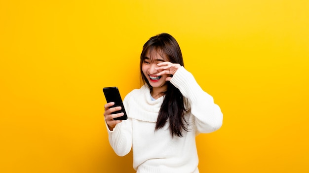 Belle fille asiatique jouant à des jeux mobiles sur un fond jaune isolé amusant et amusant pour se détendre et sourire joyeusement