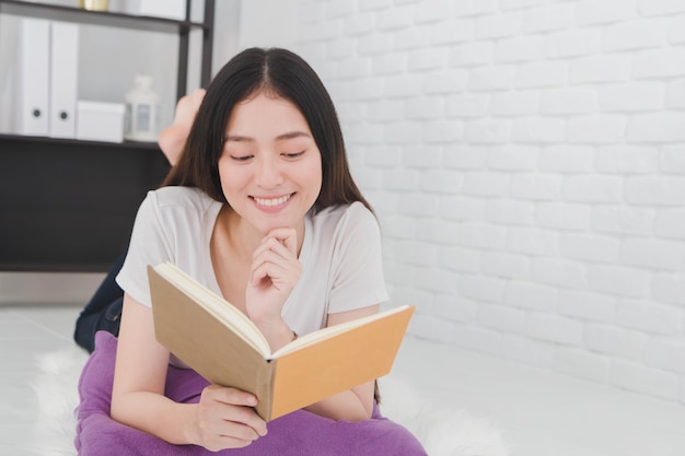 Belle fille asiatique Lire un livre sur un oreiller dans une pièce blanche à la maison