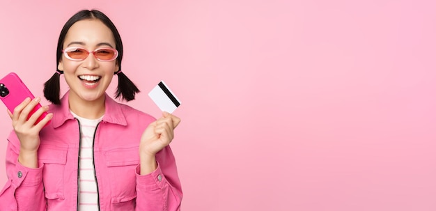 Belle fille asiatique moderne riant et souriant avec une carte de crédit de téléphone portable faisant des achats en ligne payin