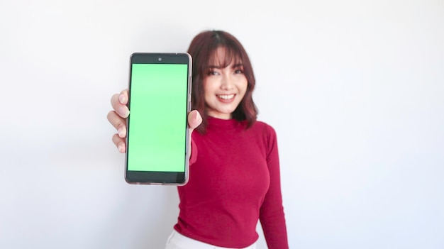 Belle fille asiatique pointe sur un téléphone à écran vert avec un arrière-plan flou sur le visage en arrière-plan blanc