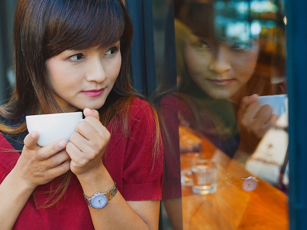 Photo belle fille asiatique en sirotant un café chaud ou latte et appuyé contre le verre avec miroir