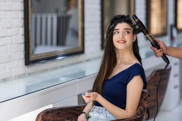 Une belle fille assise sur une chaise et souriante pendant que quelqu'un se coiffait Photo de haute qualité