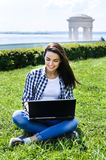 Belle fille assise dans le parc avec un ordinateur portable