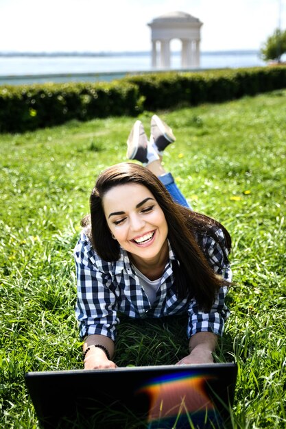 Belle fille assise dans le parc avec un ordinateur portable